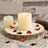 Candle on a wooden slice with dried petals on newspaper background.