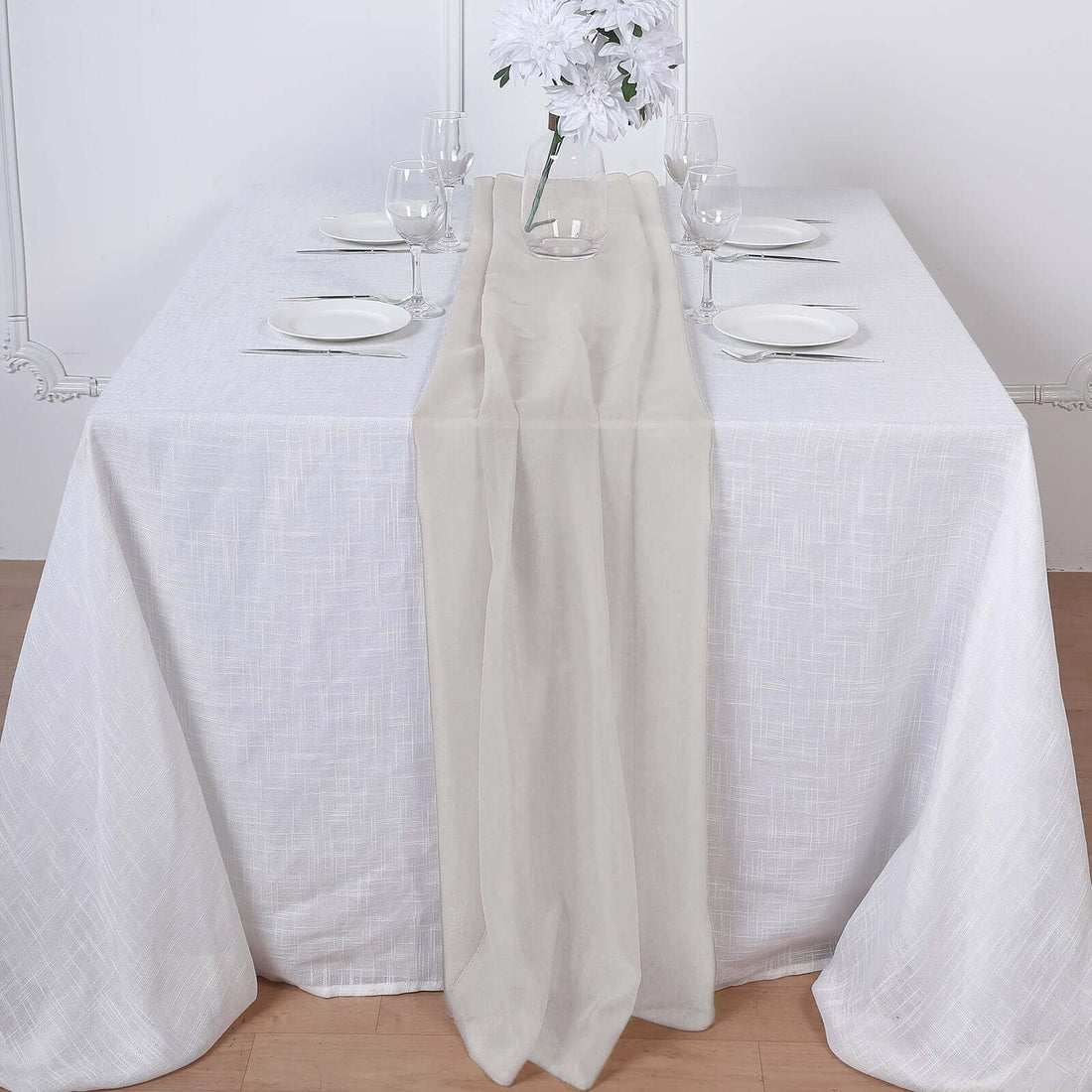 Neutral table runner on a white table setting with elegant glassware and flowers.