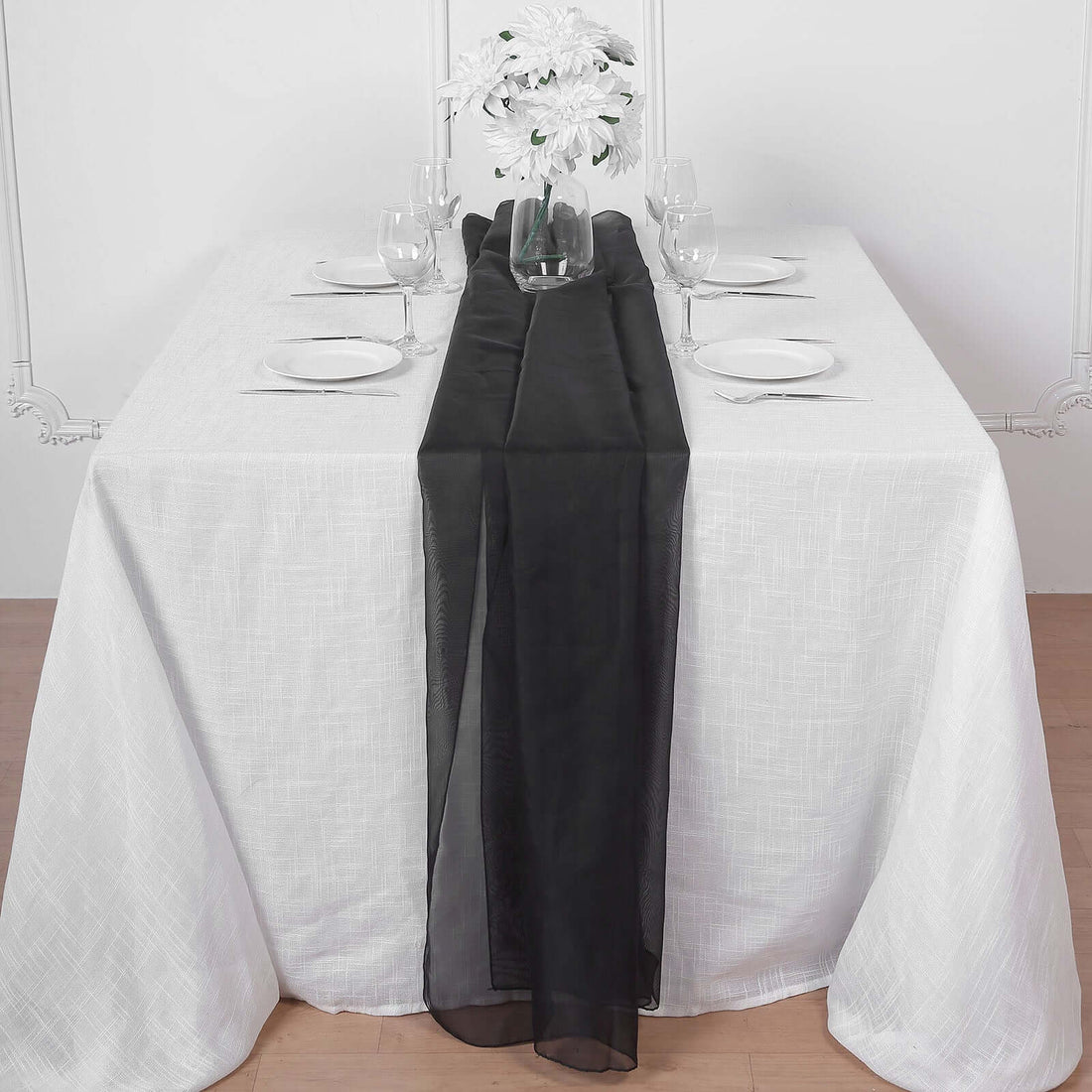 Black table runner on a white dining table set with plates and glasses.