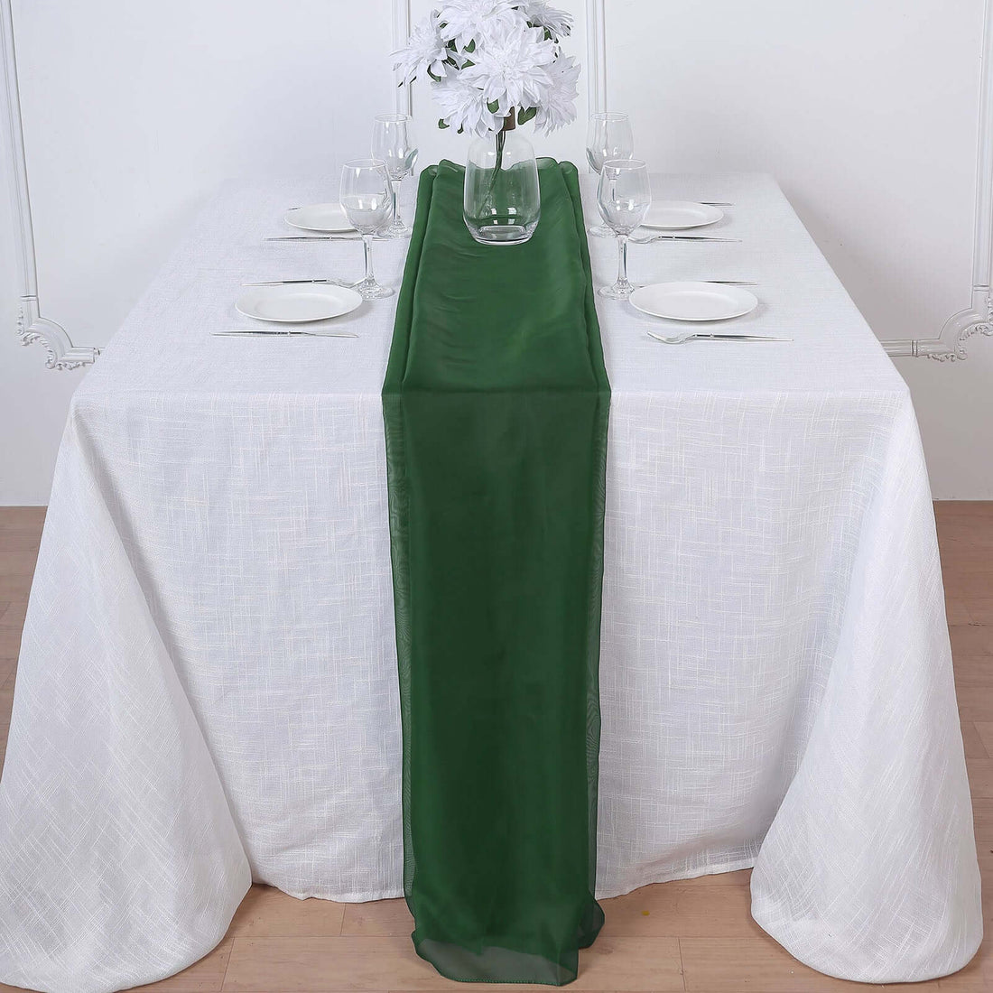 Green table runner on a white table set for dinner with glassware and plates.
