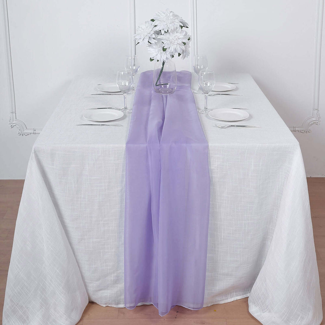 Purple table runner on a white table setting with glassware and flowers.