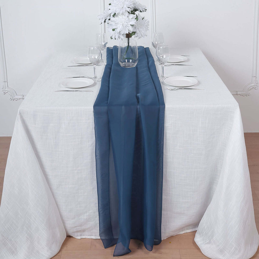Navy table runner draped elegantly on a white dining table with elegant tableware.