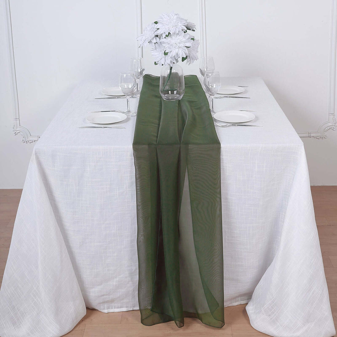 Elegant green table runner on a white table with floral centerpiece and dinnerware.