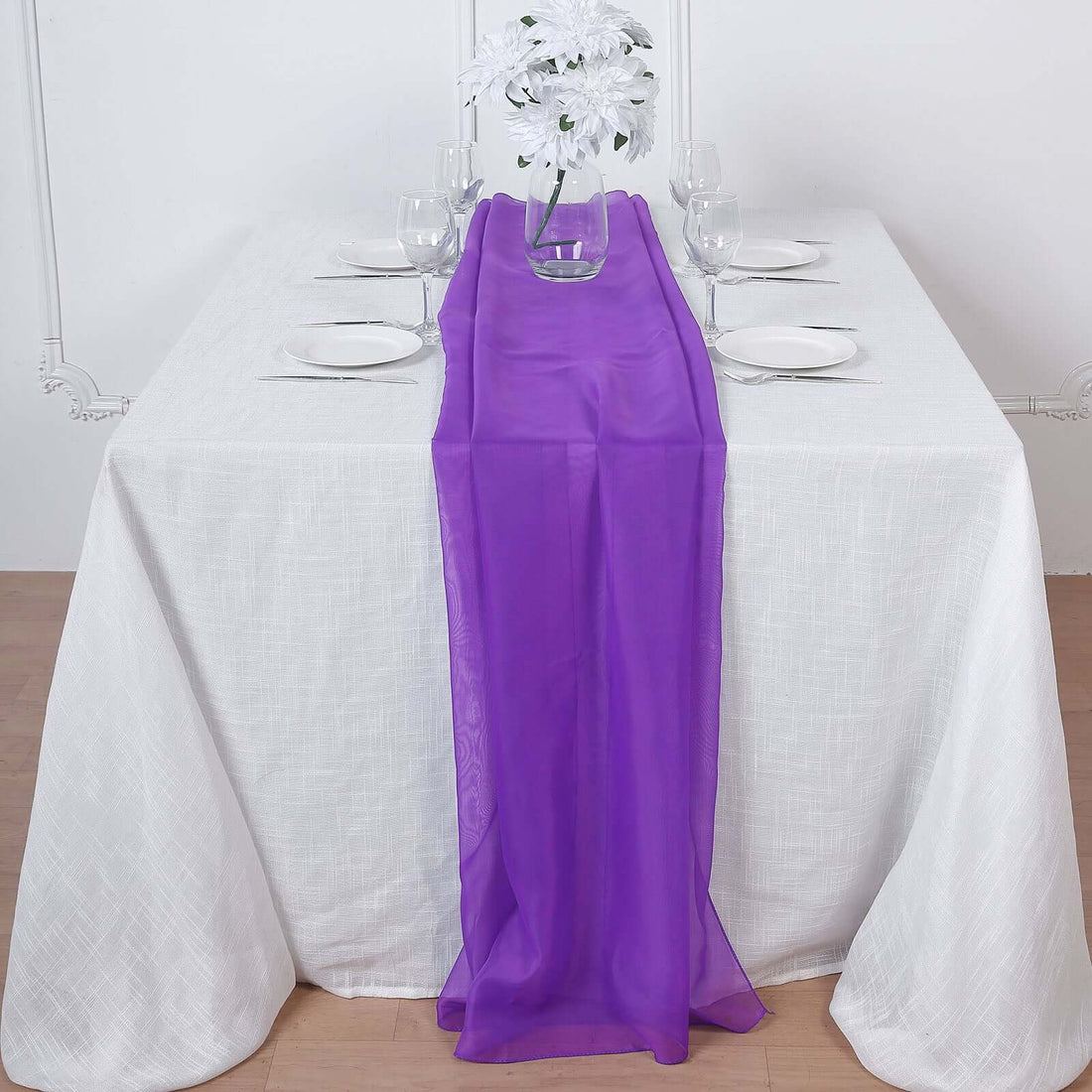 Purple table runner on a white table with glassware and flowers.