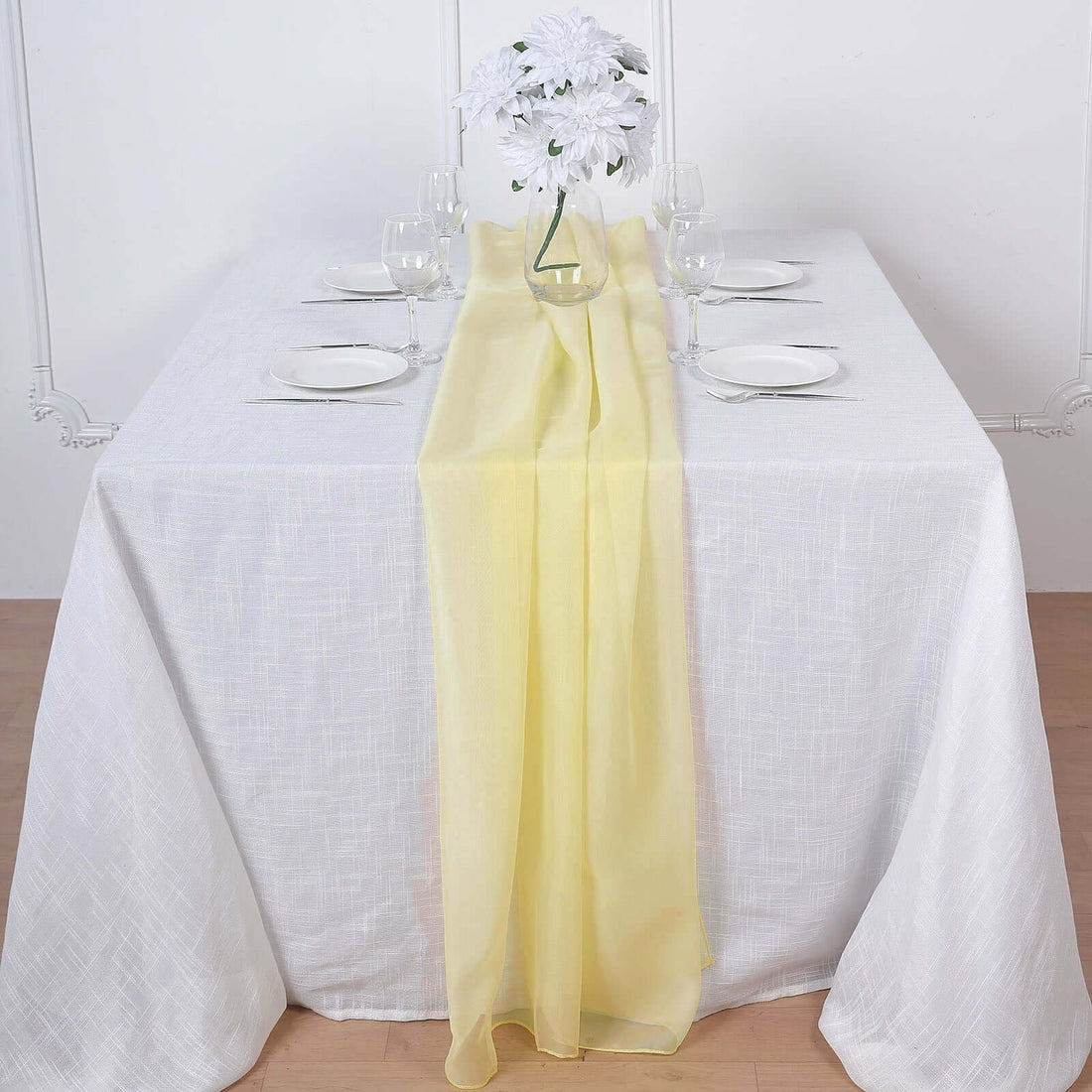 Yellow table runner on a white table setting with glassware and plates.