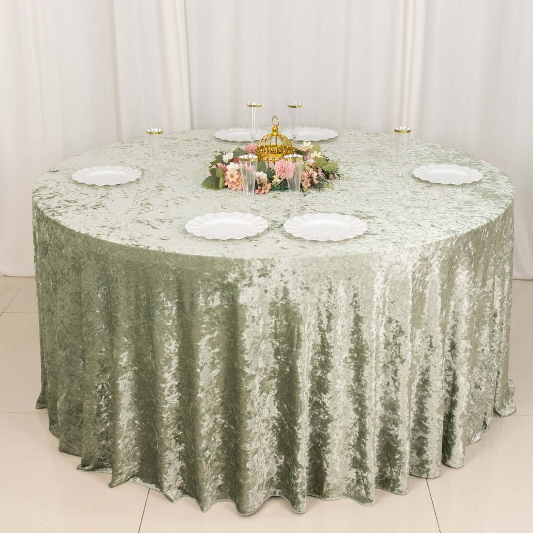 Round green velvet tablecloth with white plates and floral centerpiece.