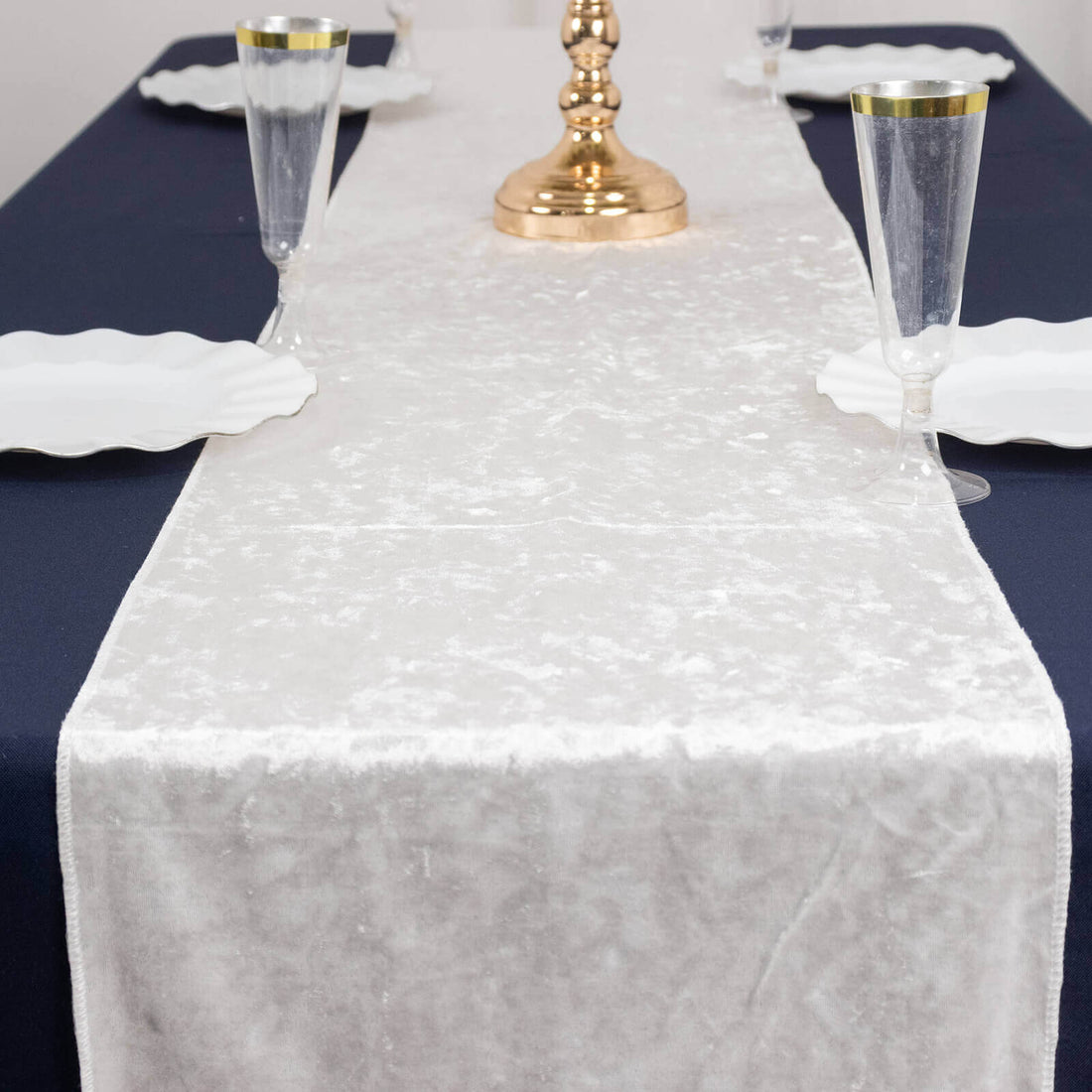Elegant white table runner on a navy table setting with glassware and plates.