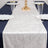 Elegant white table runner on a navy table setting with glassware and plates.