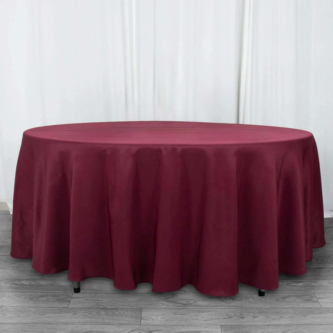 Round burgundy tablecloth on a wooden floor.