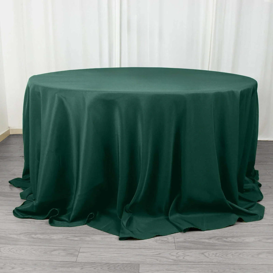 Green round tablecloth draped over a table on a wooden floor.