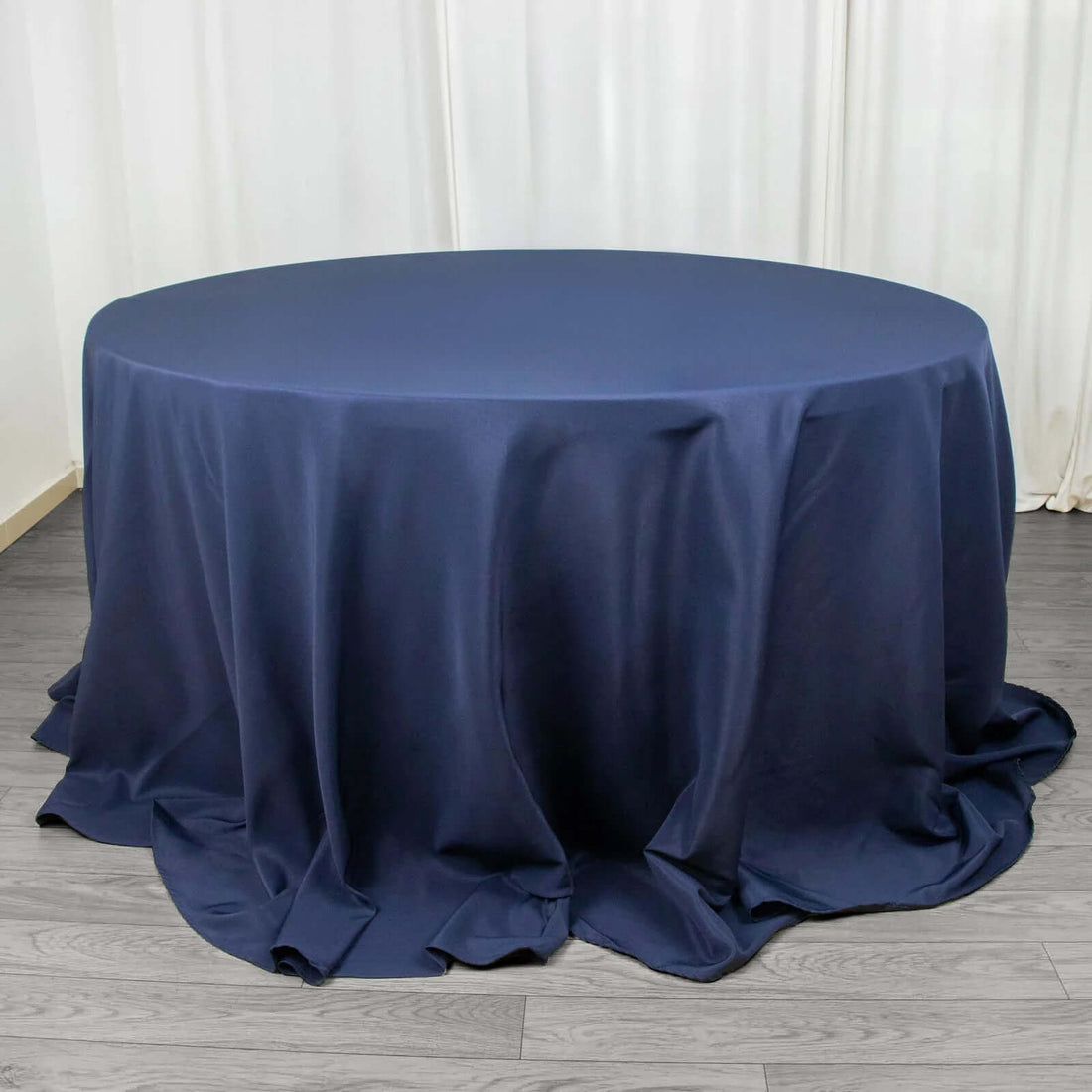 Navy round tablecloth with elegant draping on a wooden floor.