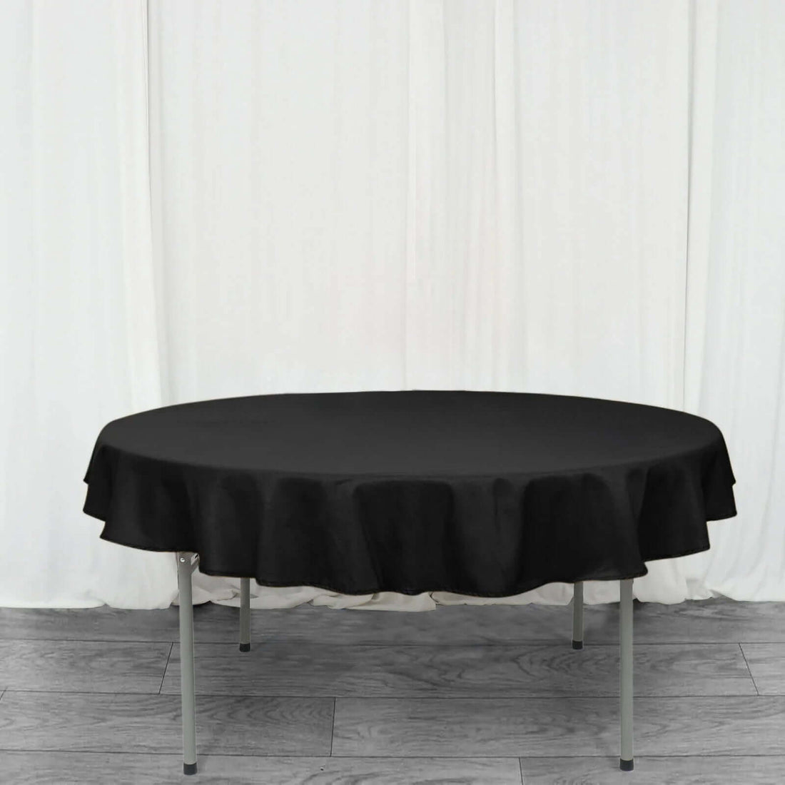 Round black tablecloth draped over a folding table against a plain backdrop.