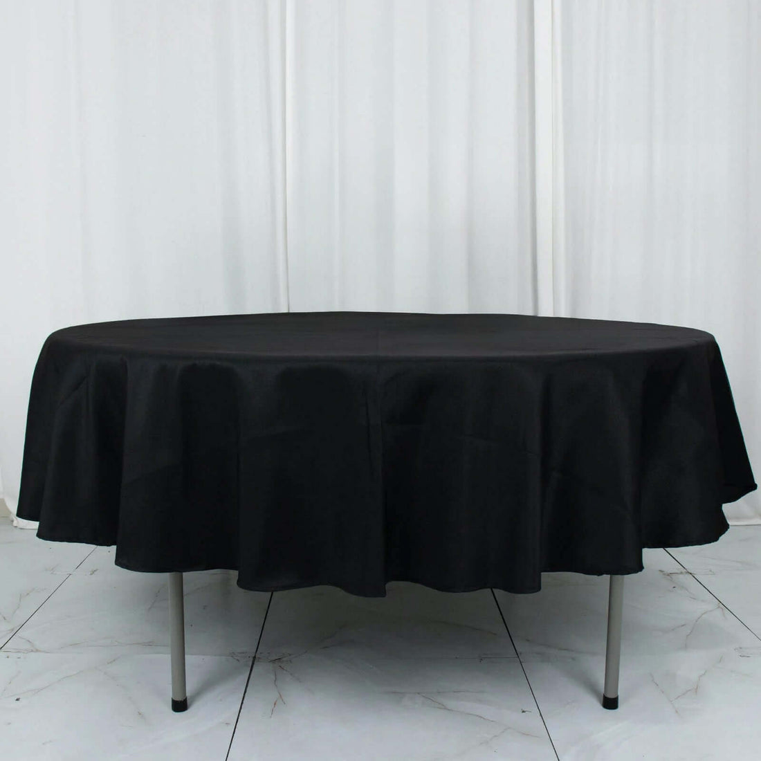 Round black tablecloth on a table with a ruffled edge.