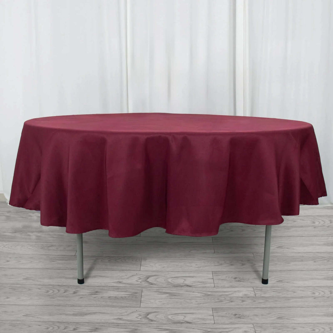 Round maroon tablecloth draped over a table in a studio setting.