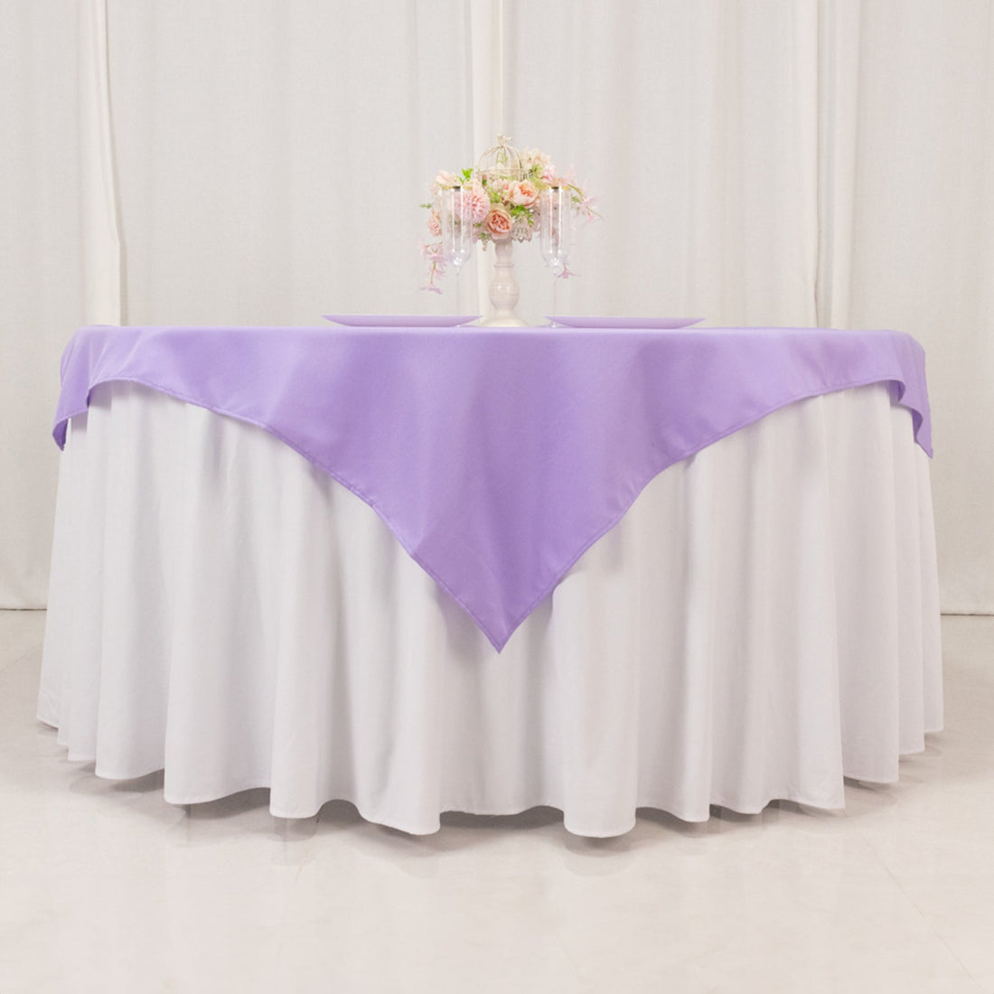 Purple tablecloth draped over a round table with floral centerpiece.