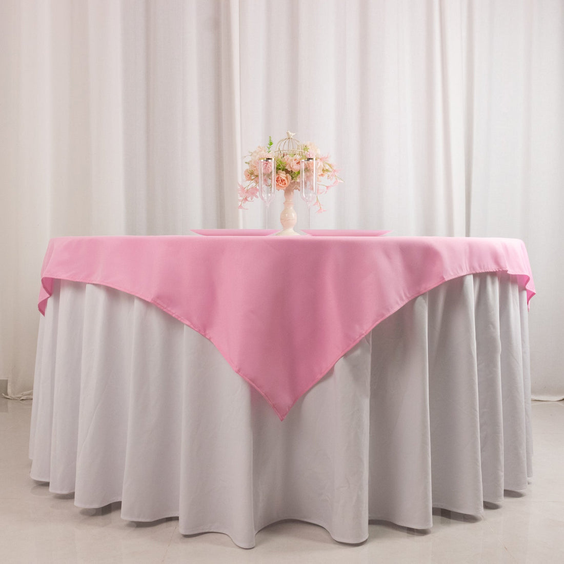 Pink tablecloth draped over a white table with floral centerpiece.