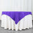 Purple tablecloth draped over a white table in a studio setting.