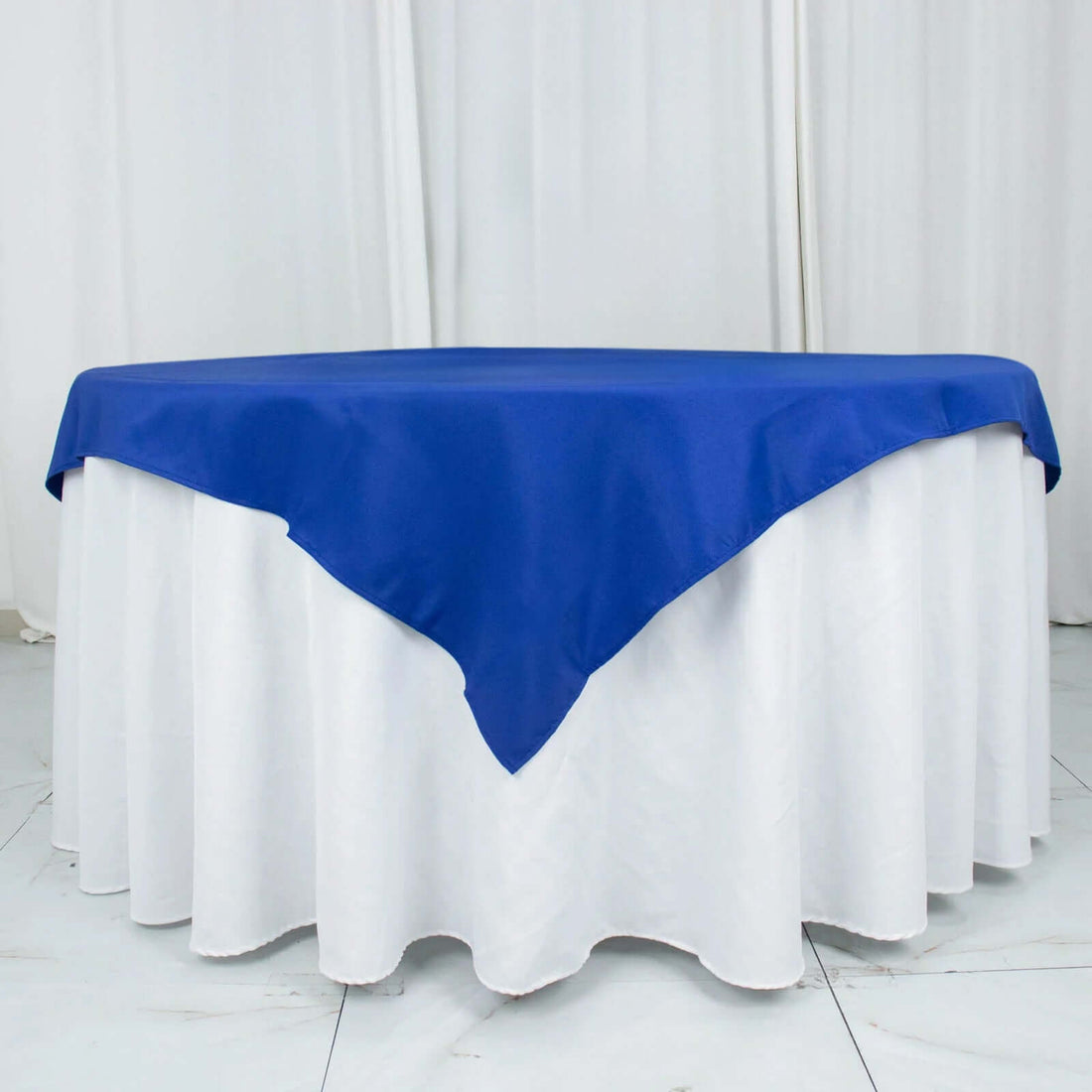 Blue tablecloth draped over a round table with white skirt.