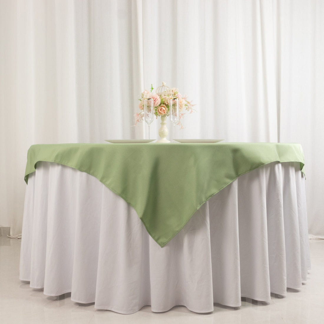 Green tablecloth draped over a round table with floral centerpiece.