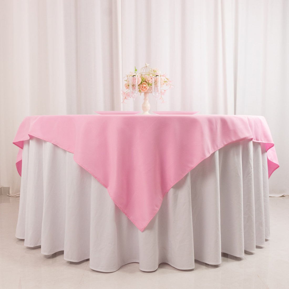 Pink tablecloth draped over a round table with floral centerpiece.