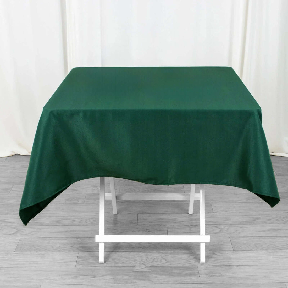Green tablecloth draped over a white folding table in a studio setting.