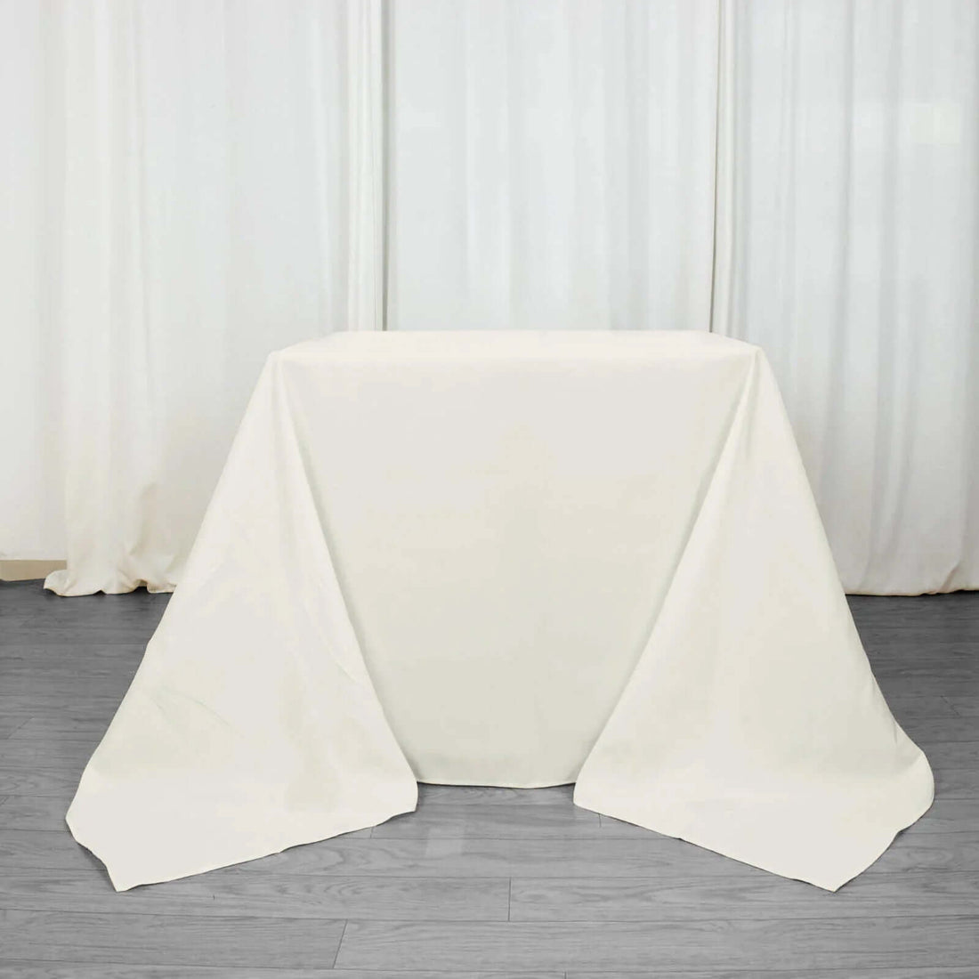 White table with draped fabric on a plain backdrop.