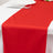 Red table runner on a white table setting with utensils and a plate.