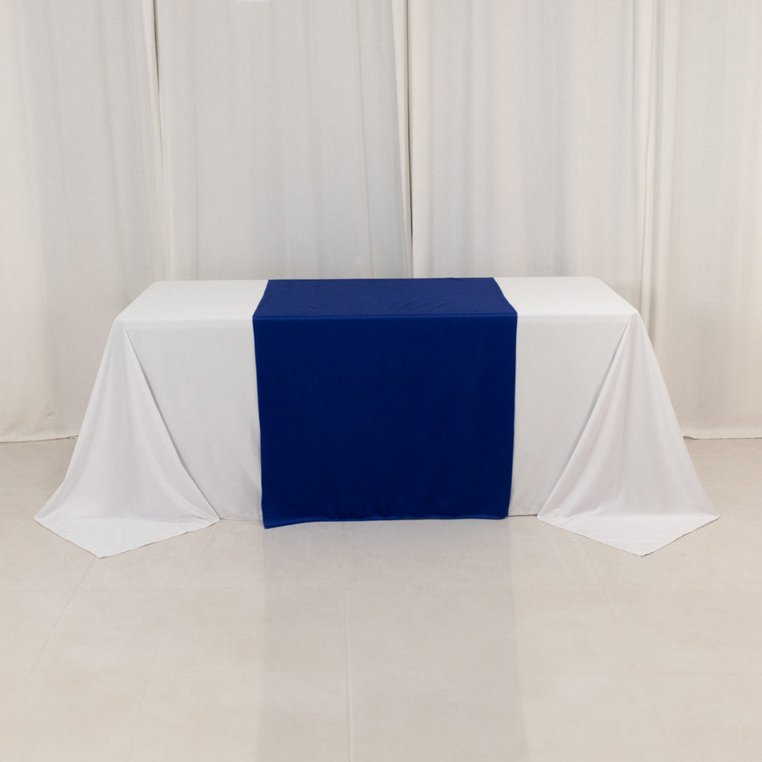 Table with white draping and a blue runner on a plain backdrop.