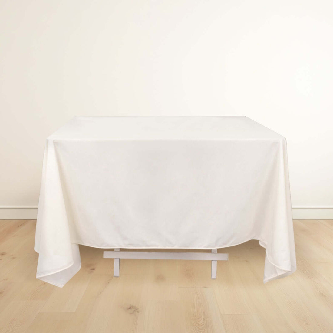 White tablecloth draped over a table on a light wooden floor.