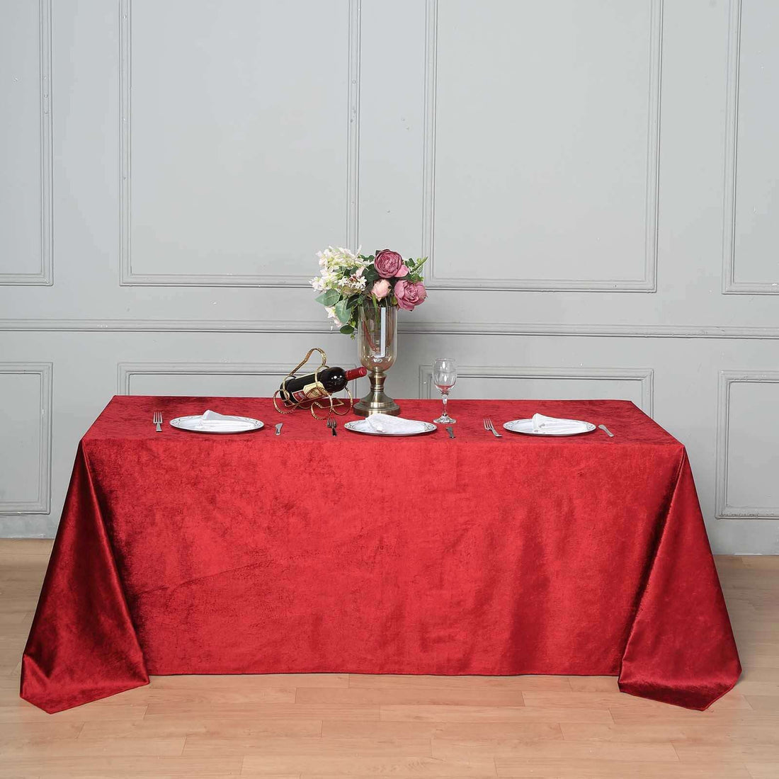 Elegant red tablecloth draped over a table set for dining with flowers and glassware.