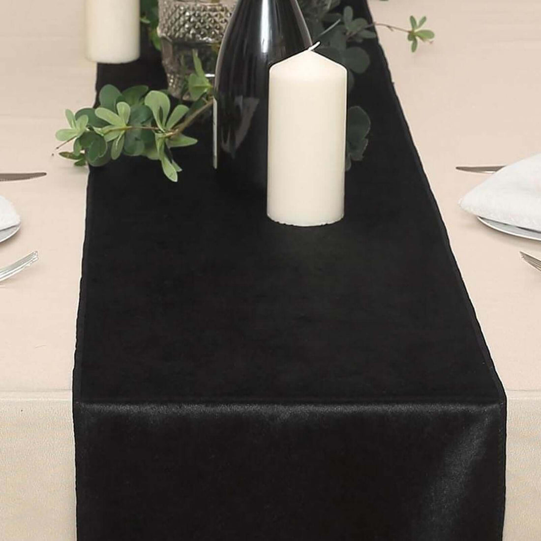 Black table runner on a dining table with candles and greenery.