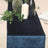 Navy velvet table runner on a beige table with greenery and candles.