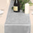 Gray velvet table runner with wine bottle and candles on a dining table.