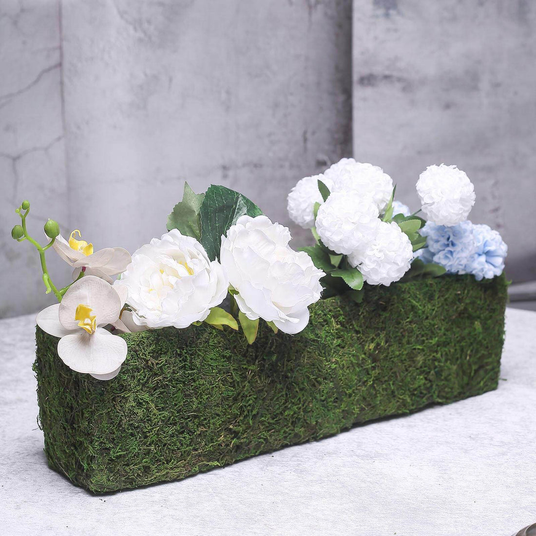 Artificial floral arrangement in a moss-covered planter.