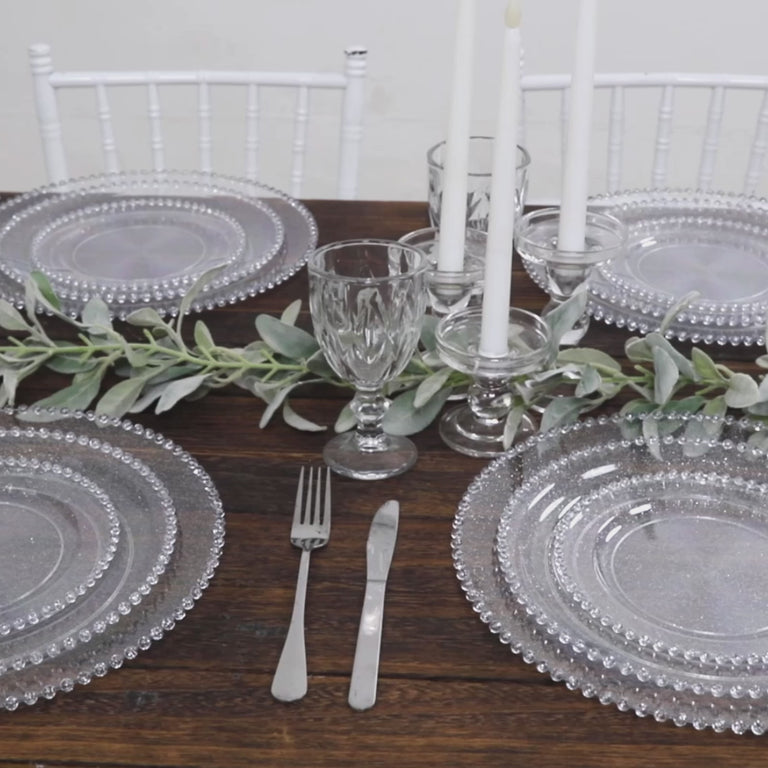 Clear silver glitter charger plates with beaded rim on a wooden table.