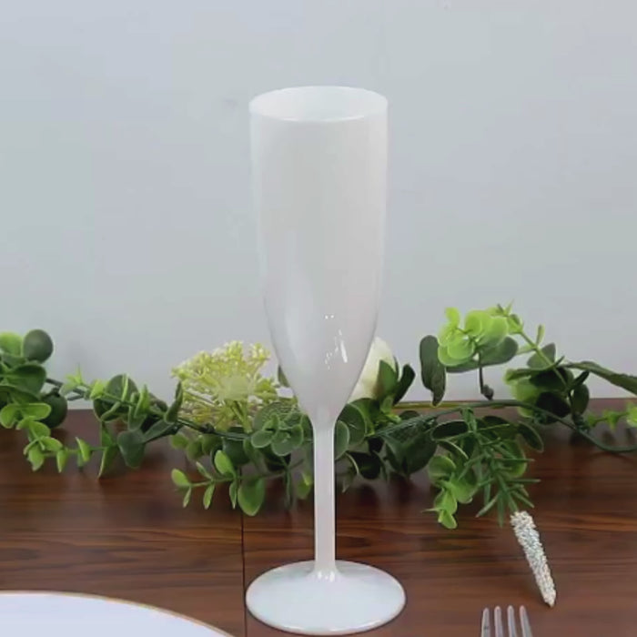 Pearl white shatterproof plastic champagne flute on a table with greenery.