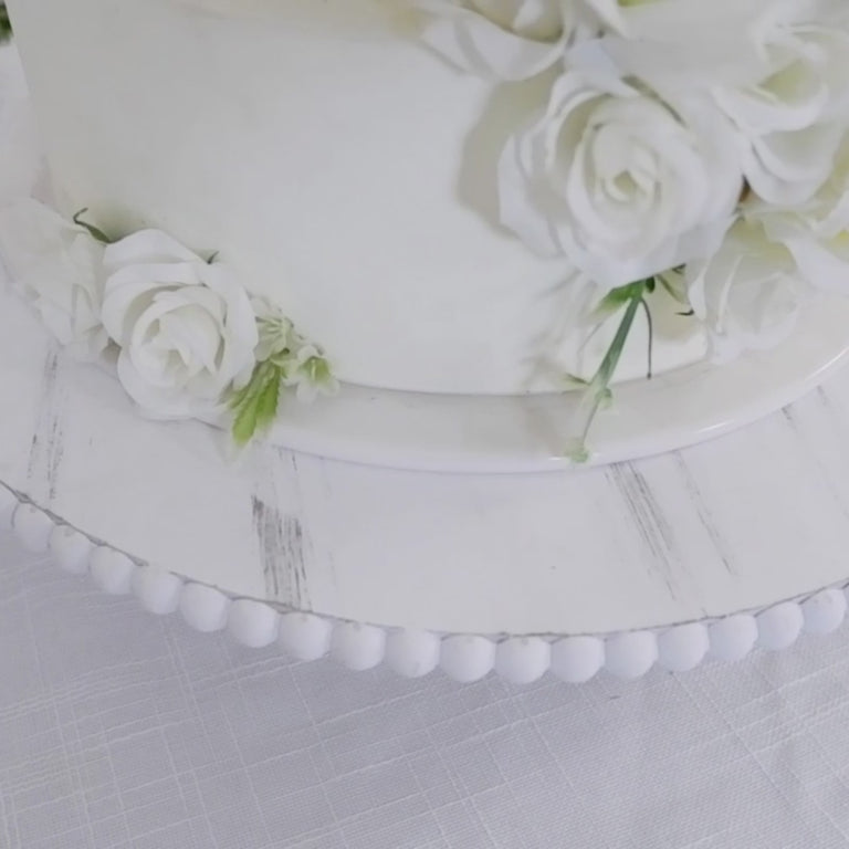Antique white wooden pedestal cake stand with beaded riser and floral accents.