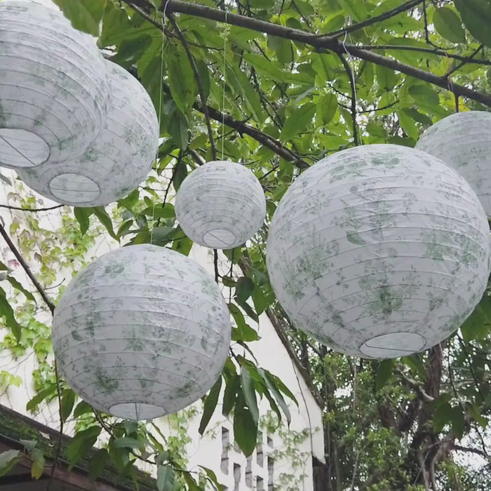 Set of 8 white sage green hanging paper lanterns in floral pattern.