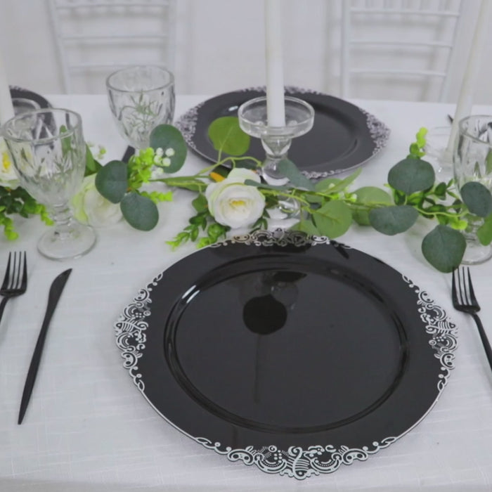 Black charger plate with silver embossed baroque rim on a dining table.