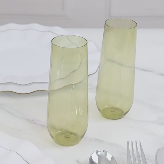 Transparent dusty sage green champagne flutes on a marble surface.