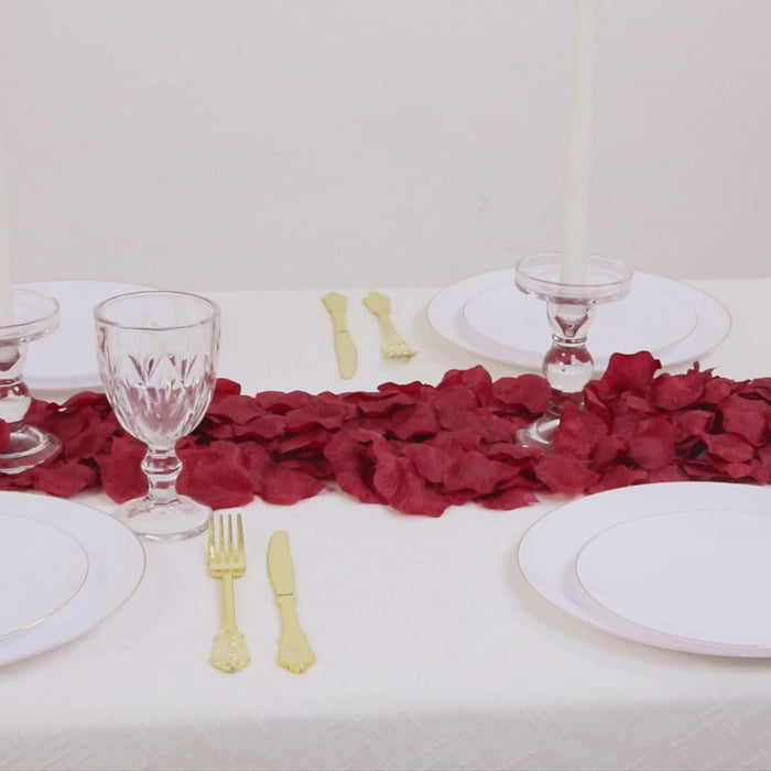 Burgundy silk rose petals scattered on a table setting.