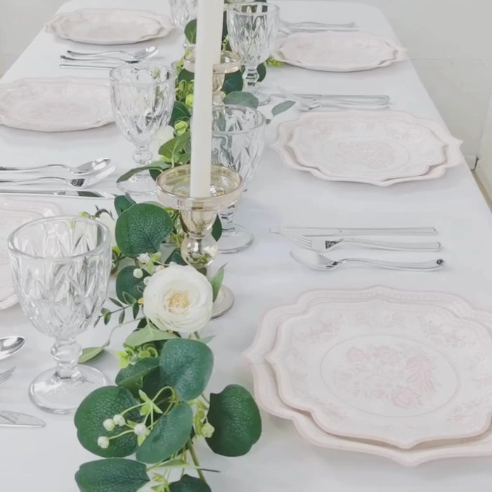 White plates with pink damask floral print on a decorated table setting.