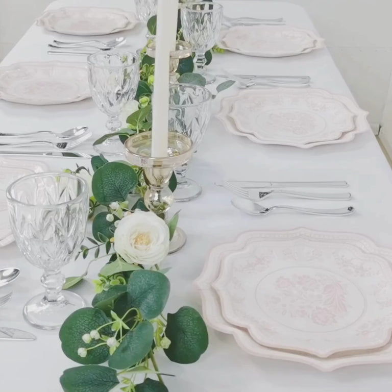 White plates with pink damask floral print on a decorated table setting.