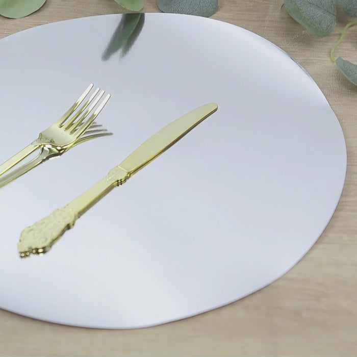 Round silver disposable placemat with gold utensils on a wooden surface.