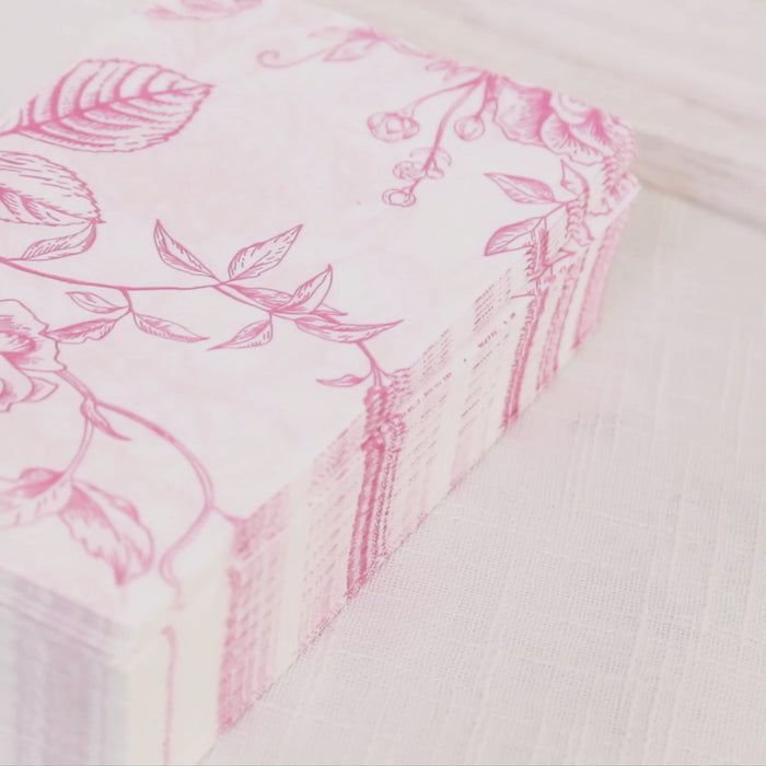 Matte pink and white floral paper cocktail napkins stacked on a light background.