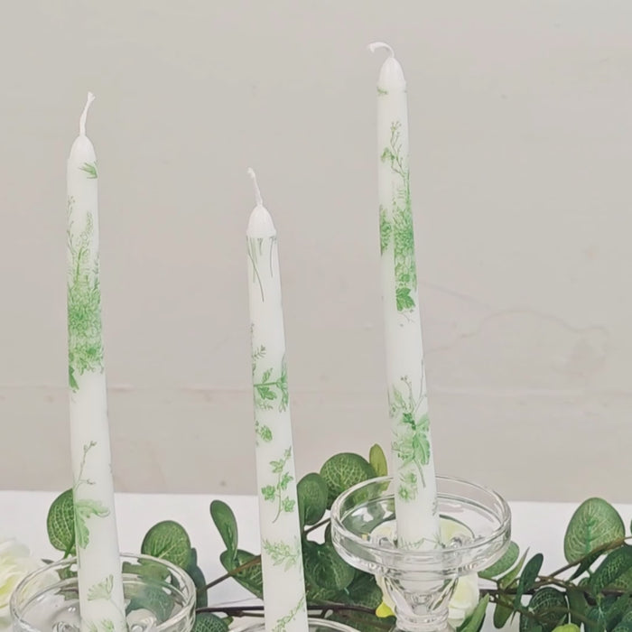 White and sage green French toile wax taper candles in a decorative setting.