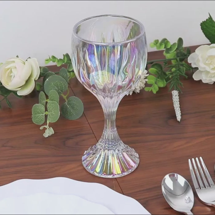 Iridescent clear wine glass goblet on a wooden table with flowers and silverware.