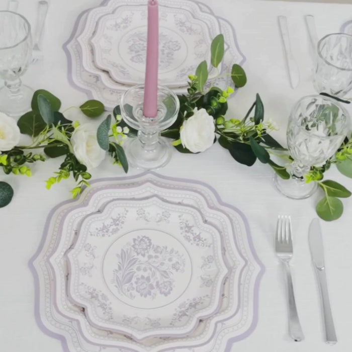 White disposable table placemats with lavender damask floral pattern and scalloped rim.