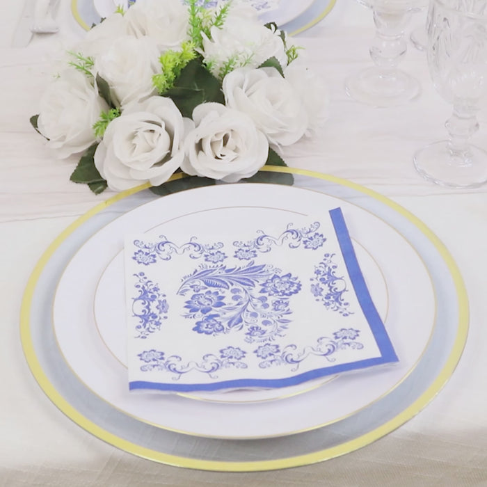 White cocktail napkin with royal blue damask pattern on a dining table setting.