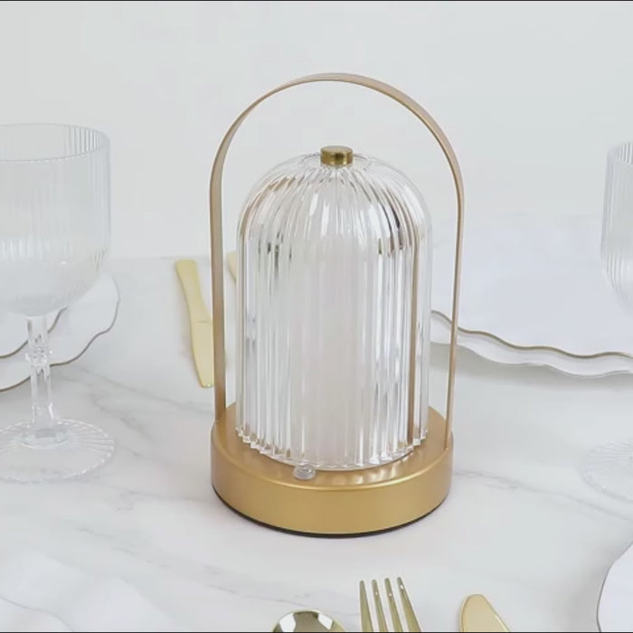 Gold cordless LED table lamp with ribbed acrylic shade on a dining table.